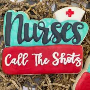 Large nurse-themed custom cookie with teal, red, and white royal icing and the phrase “Call The Shots”